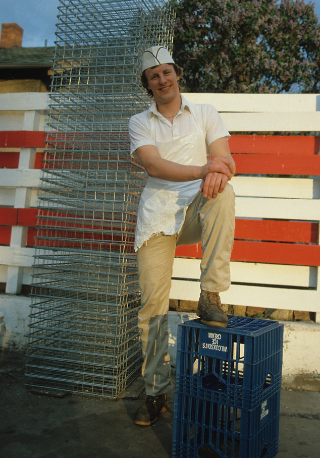 A young man in white work clothes standing by the red and white exterior of Mark's In and Out Beefburgers in Livingston Montana